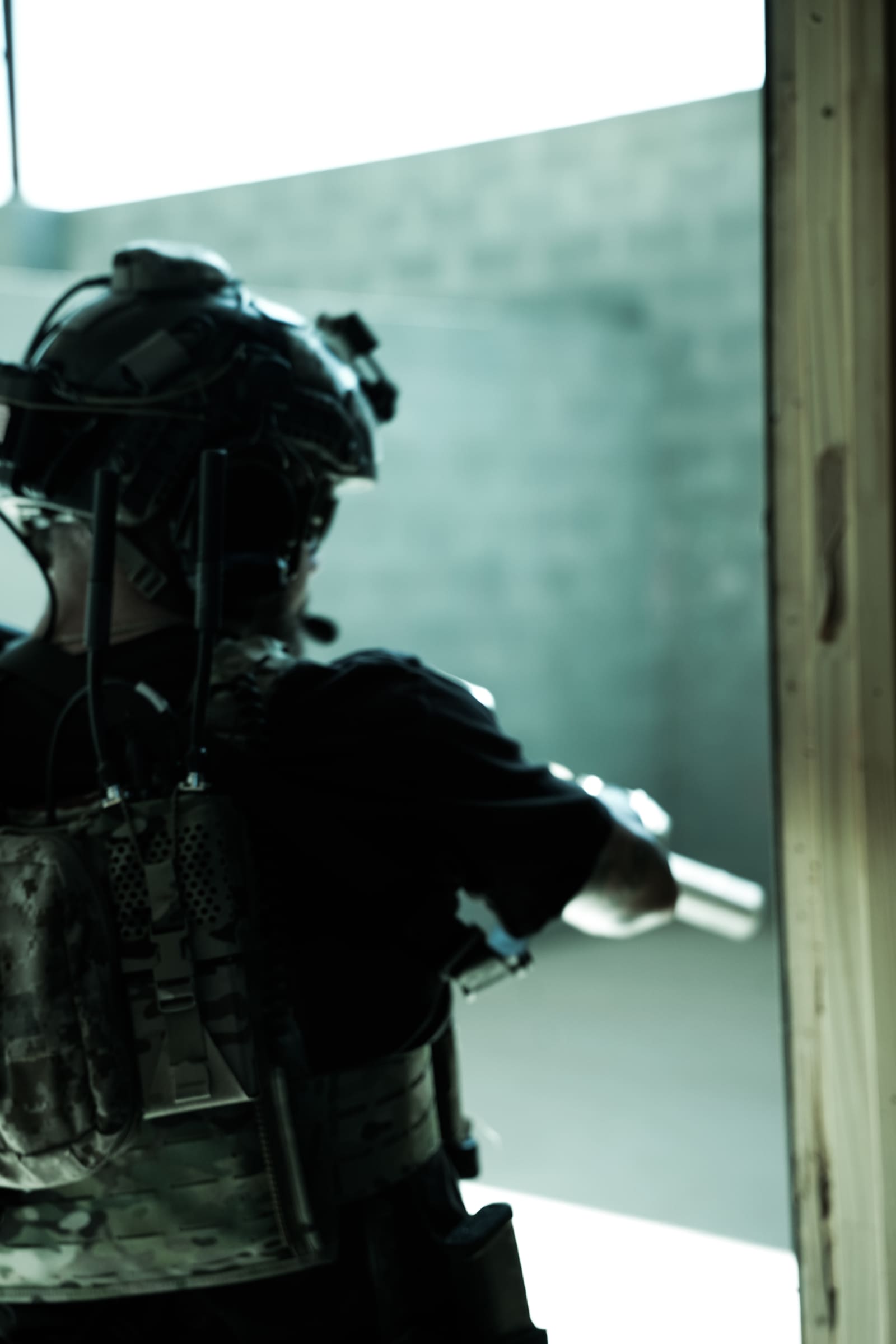Operator silhouetted against a bright doorway, rifle up