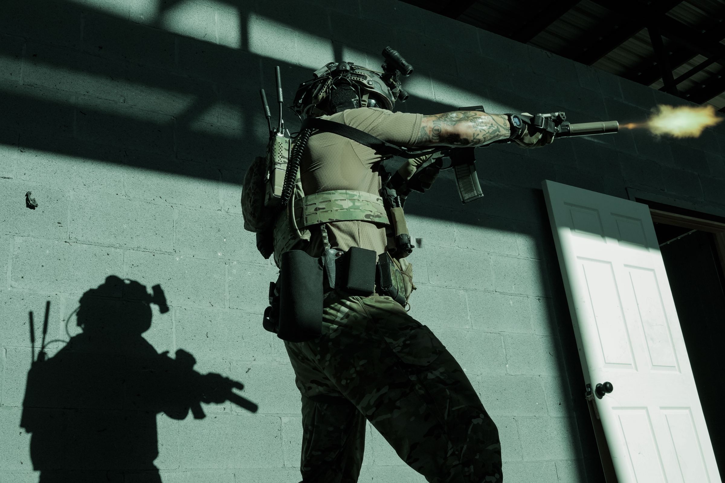 Operator firing a suppressed rifle inside a shoot house, muzzle flash lighting the wall