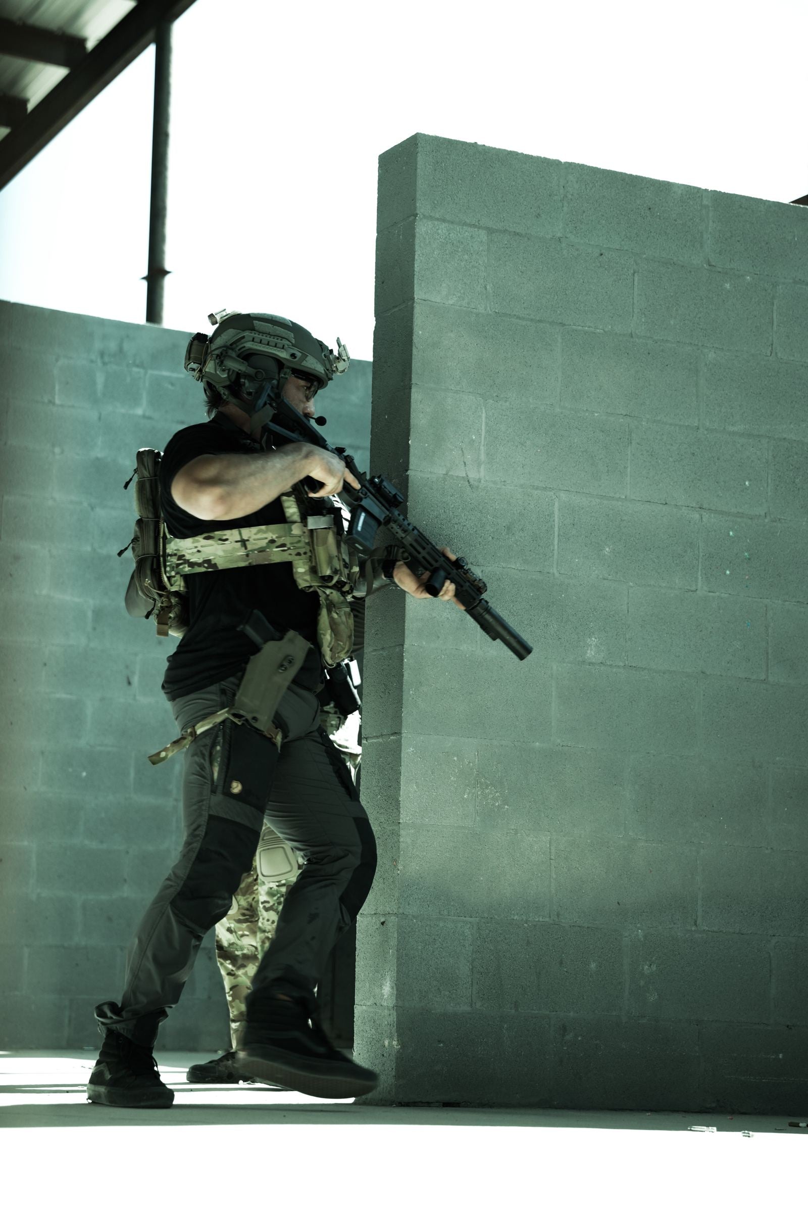 Operator advancing along a block wall with a suppressed rifle