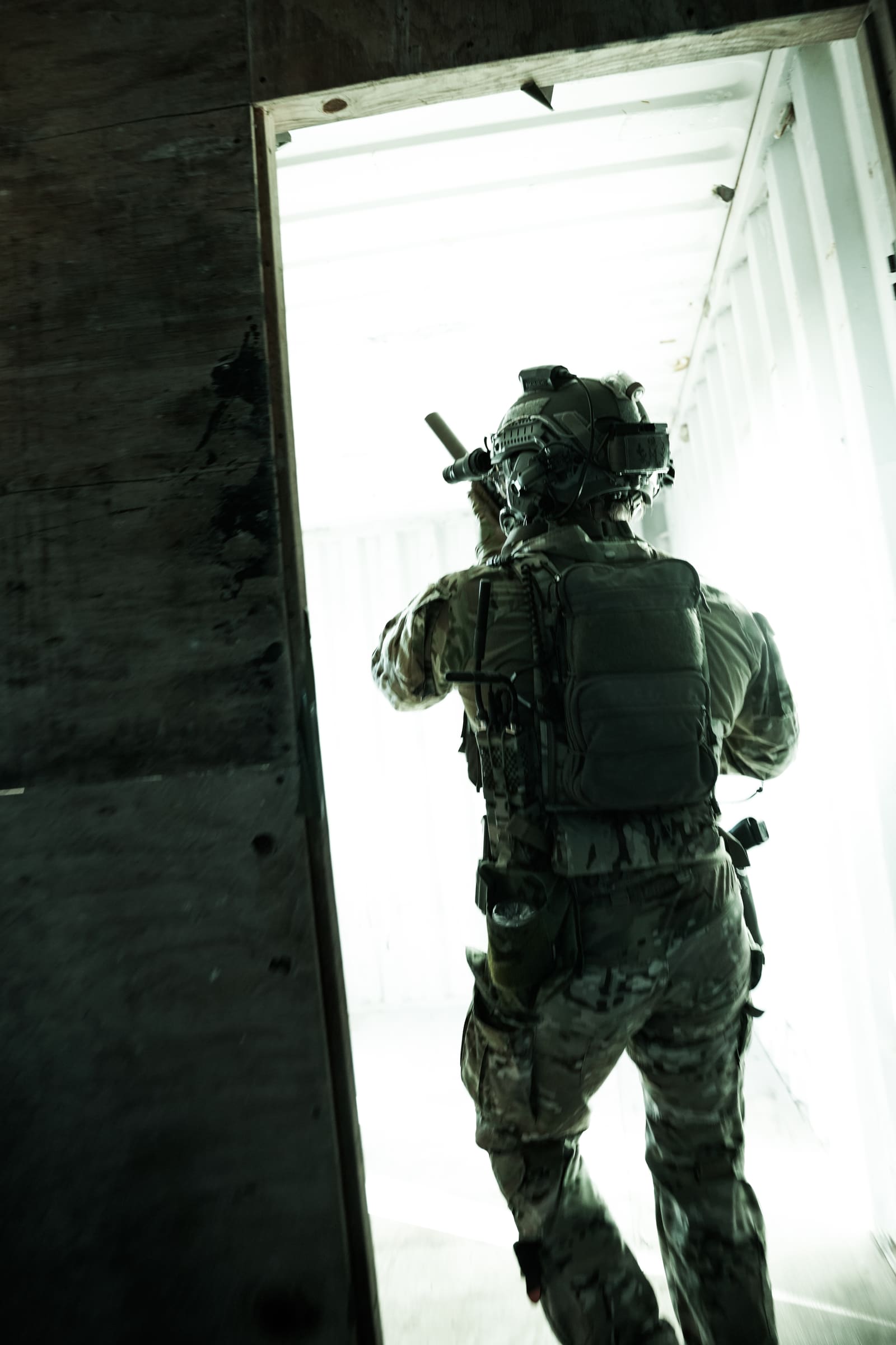 Operator moving through a breached doorway, pack and carrier square to camera